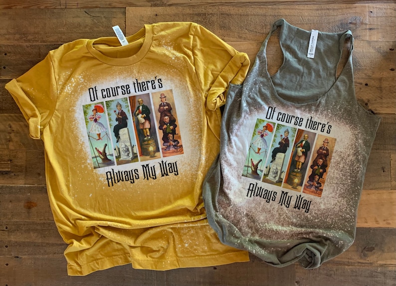 May include: Two shirts with a bleach-splattered design featuring a collage of four images of Disney characters from the Haunted Mansion ride. The text "Of course there's Always My Way" is printed on the shirts.