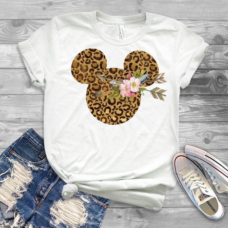 May include: White t-shirt with a leopard print Mickey Mouse head design. The Mickey Mouse head is adorned with a floral arrangement and arrows.