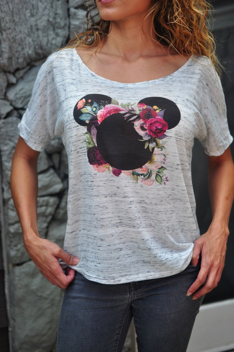 May include: A white t-shirt with a floral print of Mickey Mouse's head. The flowers are in shades of pink, red, and purple.