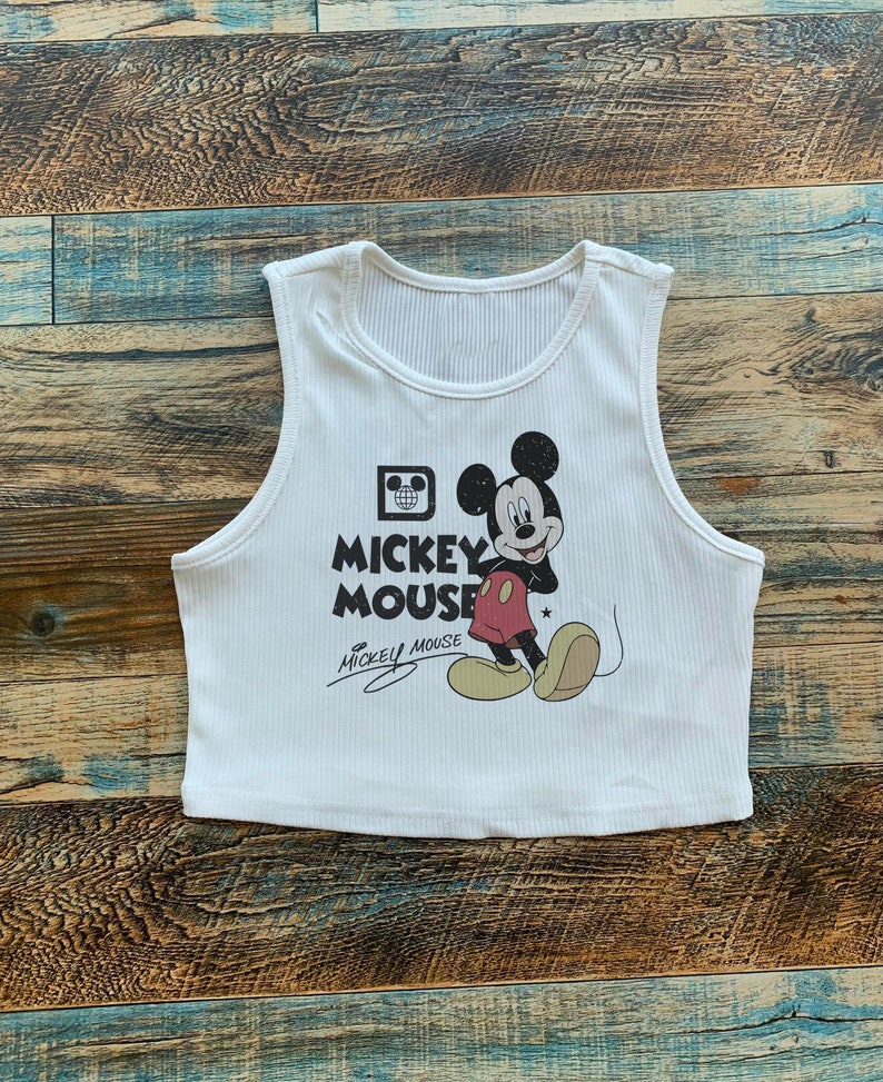 May include: White sleeveless crop top with a black and white image of Mickey Mouse and the text "Mickey Mouse" in black.