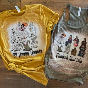 May include: Two bleached t-shirts with a Haunted Mansion theme. The yellow shirt says "99 Happy Haunts" and the green shirt says "Foolish Mortals". Both shirts feature a graphic of characters from the Haunted Mansion attraction.