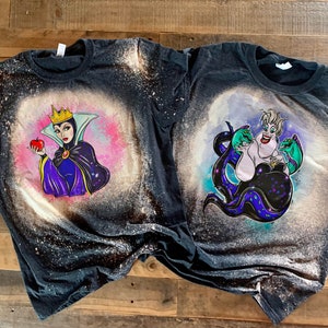 May include: Two black t-shirts with bleach designs of Disney villains. The left shirt features the Evil Queen from Snow White holding a red apple. The right shirt features Ursula from The Little Mermaid with her tentacles.