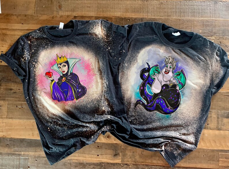 May include: Two black t-shirts with bleach designs of Disney villains. The left shirt features the Evil Queen from Snow White holding a red apple. The right shirt features Ursula from The Little Mermaid with her tentacles.