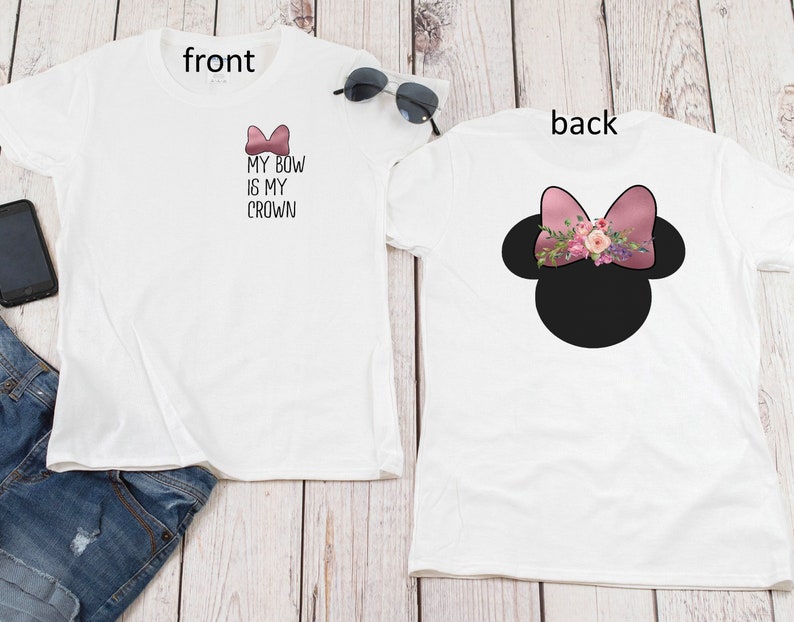 May include: White t-shirt with the text "My Bow Is My Crown" and a pink bow on the front. The back of the shirt features a black silhouette of Mickey Mouse ears with a pink bow and floral embellishments.
