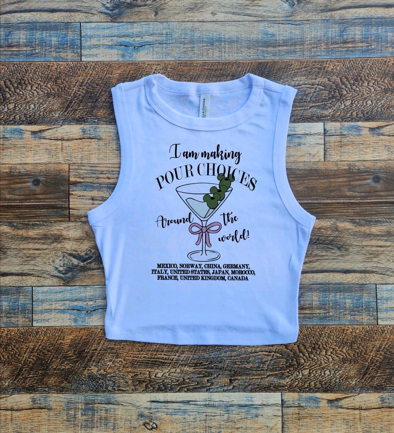 Puede incluir: Top corto blanco con el texto "I am making POUR CHOICES around the world!" y un gr&aacute;fico de copa de martini. La camiseta enumera varios pa&iacute;ses debajo del gr&aacute;fico.