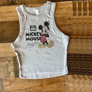 May include: A gray tank top with a vintage Mickey Mouse graphic. The graphic features Mickey Mouse in his signature red shorts and yellow shoes. The text "Mickey Mouse" is printed below the graphic.