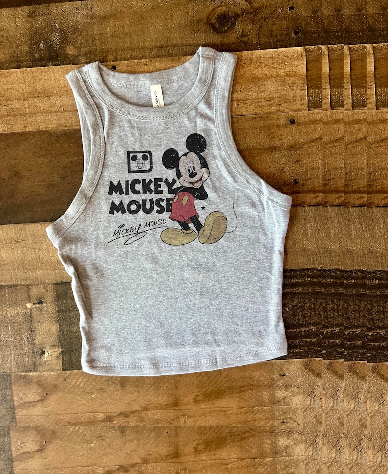 May include: A gray tank top with a vintage Mickey Mouse graphic. The graphic features Mickey Mouse in his signature red shorts and yellow shoes. The text "Mickey Mouse" is printed below the graphic.