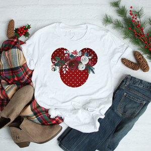 May include: White t-shirt with a red and white polka dot Mickey Mouse head design featuring a floral arrangement of red, white, and burgundy flowers.