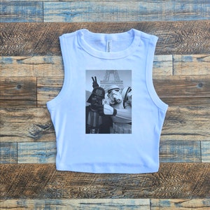 May include: A light blue sleeveless crop top with a black and white graphic print of Darth Vader, a Stormtrooper, and a Rebel Trooper taking a selfie in front of the Eiffel Tower.