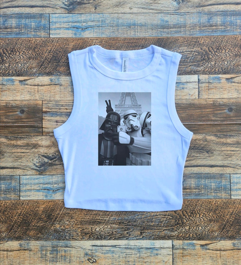 May include: A light blue sleeveless crop top with a black and white graphic print of Darth Vader, a Stormtrooper, and a Rebel Trooper taking a selfie in front of the Eiffel Tower.