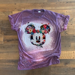 May include: Purple t-shirt with a bleach-splattered design featuring a floral Mickey Mouse head.