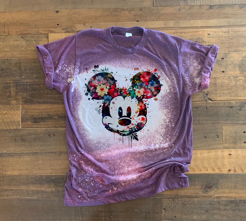 May include: Purple t-shirt with a bleach-splattered design featuring a floral Mickey Mouse head.
