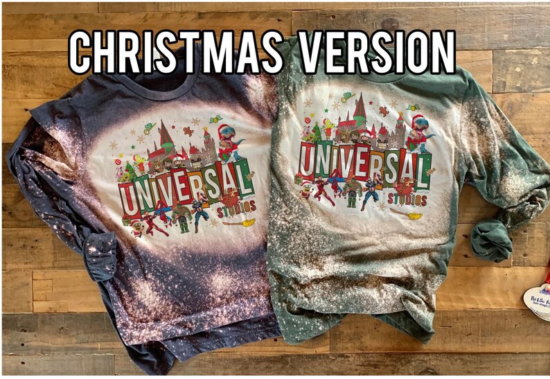 May include: Two long-sleeved shirts with a bleach-splattered design featuring a Christmas-themed Universal Studios logo. The shirts are in dark blue and green.