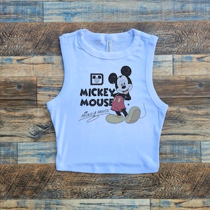 May include: White sleeveless crop top with a vintage Mickey Mouse graphic and the text "Mickey Mouse" in black lettering.