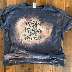 May include: A blue t-shirt with a bleach-splattered design featuring the words "Mother Mom Mommy Mama Madre" in a gold frame with floral accents.