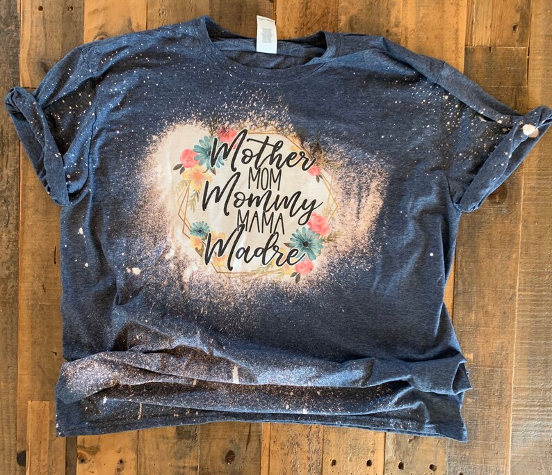 May include: A blue t-shirt with a bleach-splattered design featuring the words "Mother Mom Mommy Mama Madre" in a gold frame with floral accents.