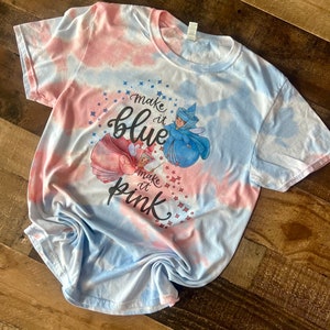 May include: A tie-dye t-shirt with a blue and pink color scheme. The shirt features a graphic of two fairies with the text "Make it blue" and "Make it pink".