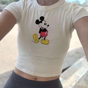 フットボールミッキーベビーTシャツ、秋のフットボール、スポーツディズニーパンプキンシャツ、季節の到来、ユニセックスブリーチチャコール、 Cream Baby Tee