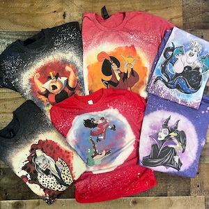 May include: Six different t-shirts with bleach-splattered designs featuring various Disney villains. The villains include Ursula, Maleficent, Cruella de Vil, Jafar, the Queen of Hearts, and Captain Hook.