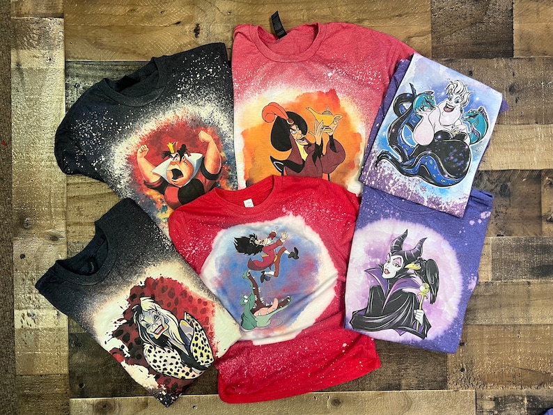 May include: Six different t-shirts with bleach-splattered designs featuring various Disney villains. The villains include Ursula, Maleficent, Cruella de Vil, Jafar, the Queen of Hearts, and Captain Hook.