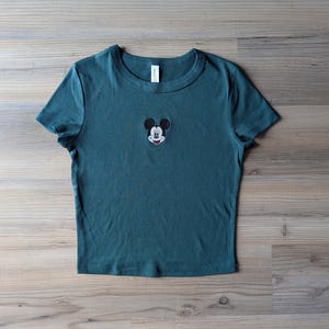 May include: A white ceramic mug with a black handle and the text "But First, Coffee" in a bold, black font. The mug is set against a blurred background, suggesting a cozy setting. The mug appears to be approximately 4 inches tall.