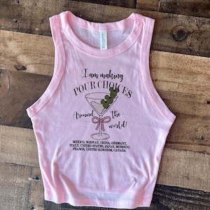 Puede incluir: Una camiseta sin mangas rosa claro de Bella + Canvas con el texto "I am making POUR CHOICES around the world!" y un gr&aacute;fico de copa de martini. La parte inferior de la camisa enumera varios pa&iacute;ses.