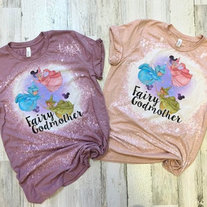 May include: Two bleached t-shirts with a graphic of three fairies and the text "Fairy Godmother". The shirts are in shades of pink and brown.