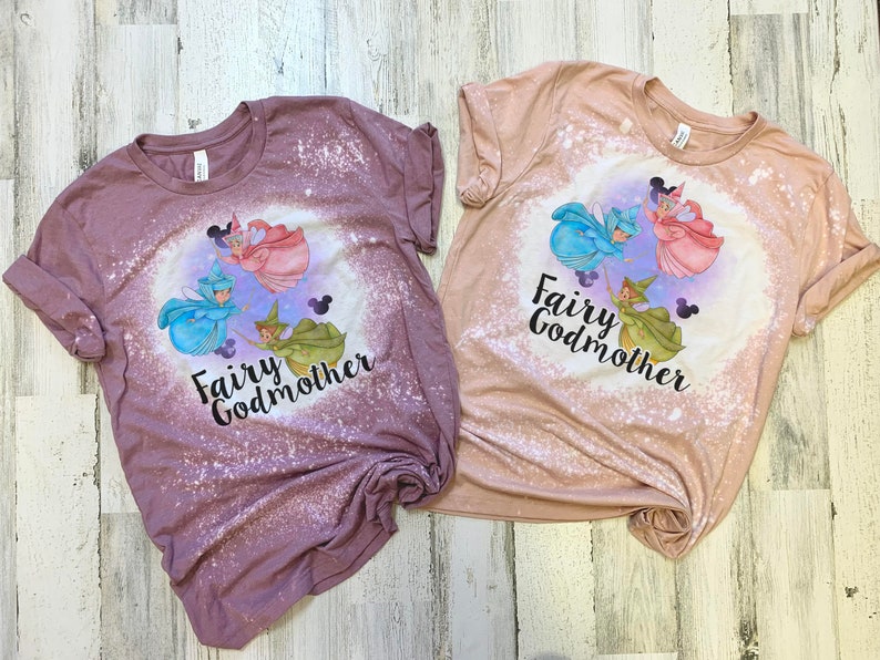 May include: Two bleached t-shirts with a graphic of three fairies and the text "Fairy Godmother". The shirts are in shades of pink and brown.