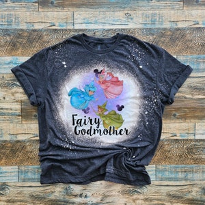 May include: A dark gray t-shirt with a bleach-splattered design featuring three fairies with wands and the text "Fairy Godmother".