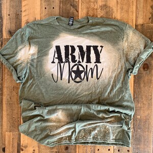 May include: A green t-shirt with a bleach-splattered design. The shirt has the words "Army Mom" printed in black with a star.