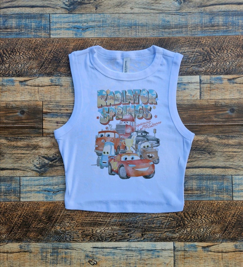 May include: White sleeveless crop top with a graphic print of the Cars characters from the movie Cars. The graphic includes the text "Radiator Springs" and "Lightning McQueen".