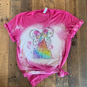 May include: Pink t-shirt with a bleach-splattered design featuring a rainbow-colored castle with Mickey Mouse ears and fireworks.