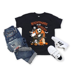 May include: Black t-shirt with a graphic of Jack Skellington from Nightmare Before Christmas, with the text "Nightmare on Main Street". The shirt is paired with blue jeans and white sneakers with black stripes.