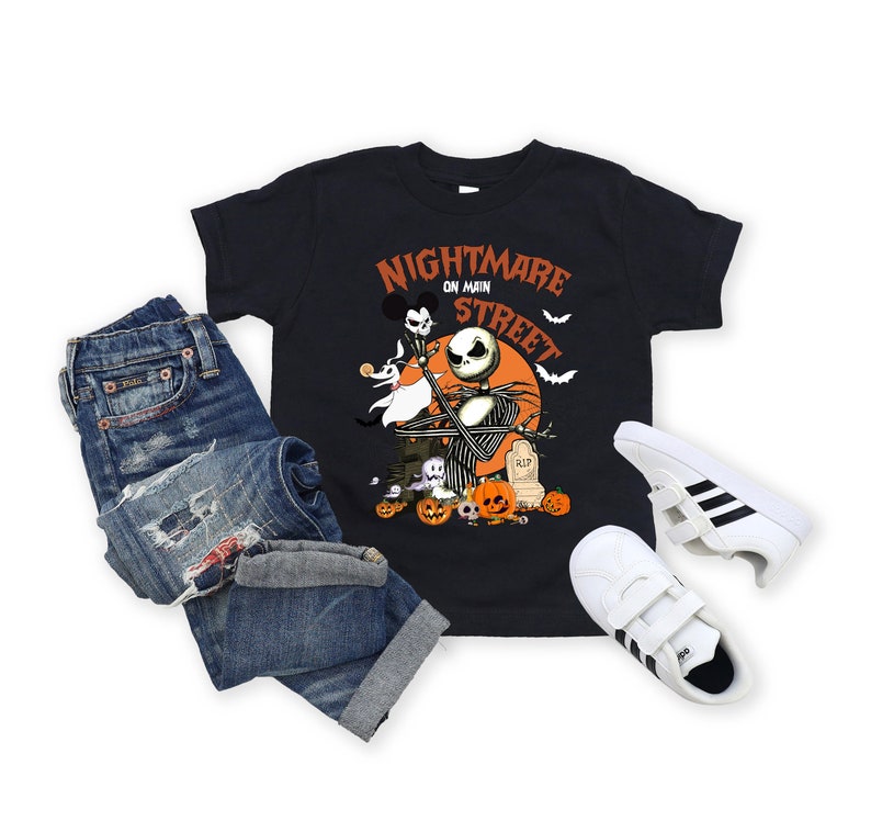 May include: Black t-shirt with a graphic of Jack Skellington from Nightmare Before Christmas, with the text "Nightmare on Main Street". The shirt is paired with blue jeans and white sneakers with black stripes.