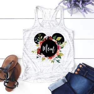 May include: White tank top with a black Mickey Mouse head silhouette surrounded by watercolor flowers. The word "Mom" is written in black inside the circle of the head.
