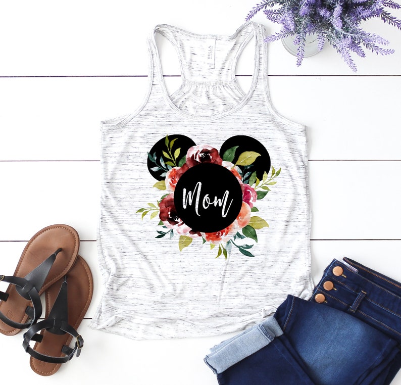 May include: White tank top with a black Mickey Mouse head silhouette surrounded by watercolor flowers. The word "Mom" is written in black inside the circle of the head.