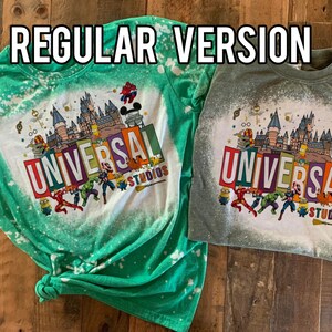 May include: Two bleached t-shirts featuring a graphic print of the Universal Studios logo and various cartoon characters. The text "UNIVERSAL STUDIOS" is printed on the shirts. The shirts are green and grey.