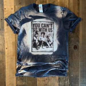 May include: A blue t-shirt with a bleached design featuring a picture of three witches from the movie Hocus Pocus. The text "You Can't Sit With Us" is printed on the shirt.