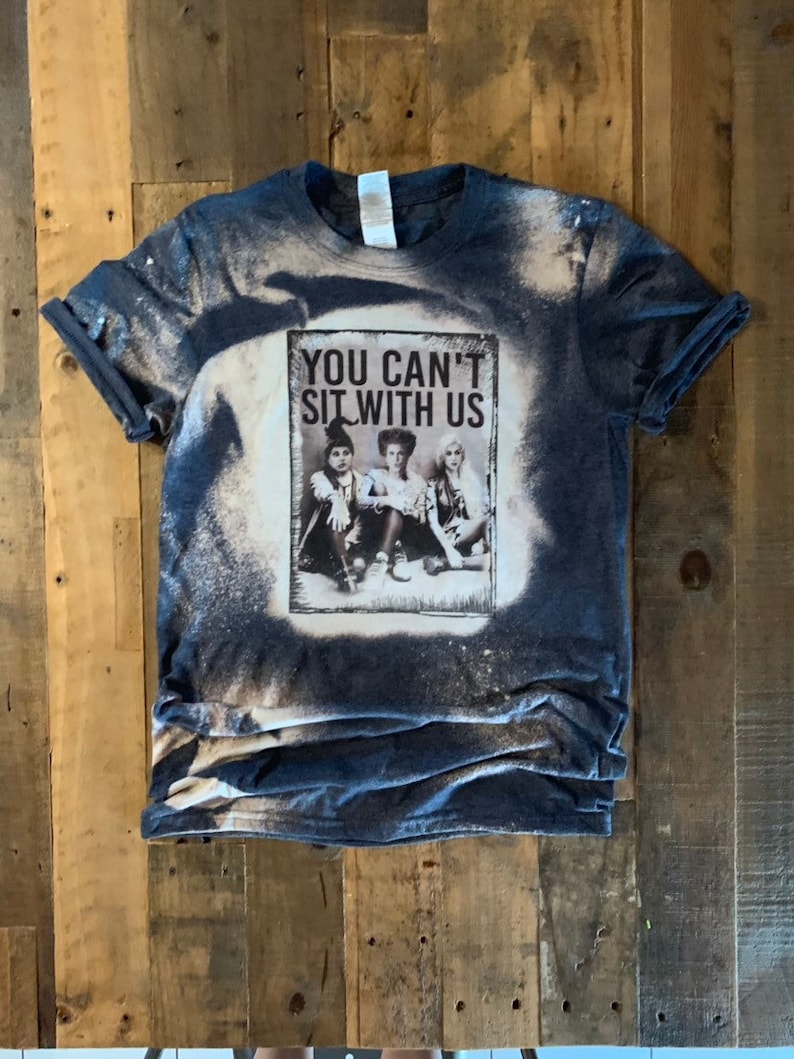 May include: A blue t-shirt with a bleached design featuring a picture of three witches from the movie Hocus Pocus. The text "You Can't Sit With Us" is printed on the shirt.