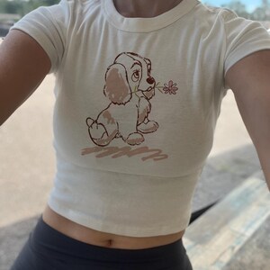 レディ・アンド・トランプのクロップタンク、パピーベビーTシャツ、映画版アメリカン・コッカー・スパニエル、レトロなディズニー・ドッグ、イングリッシュ・ドッグ、ディズニーワールドTシャツ、ディズニーランドTシャツ Cream Baby Tee