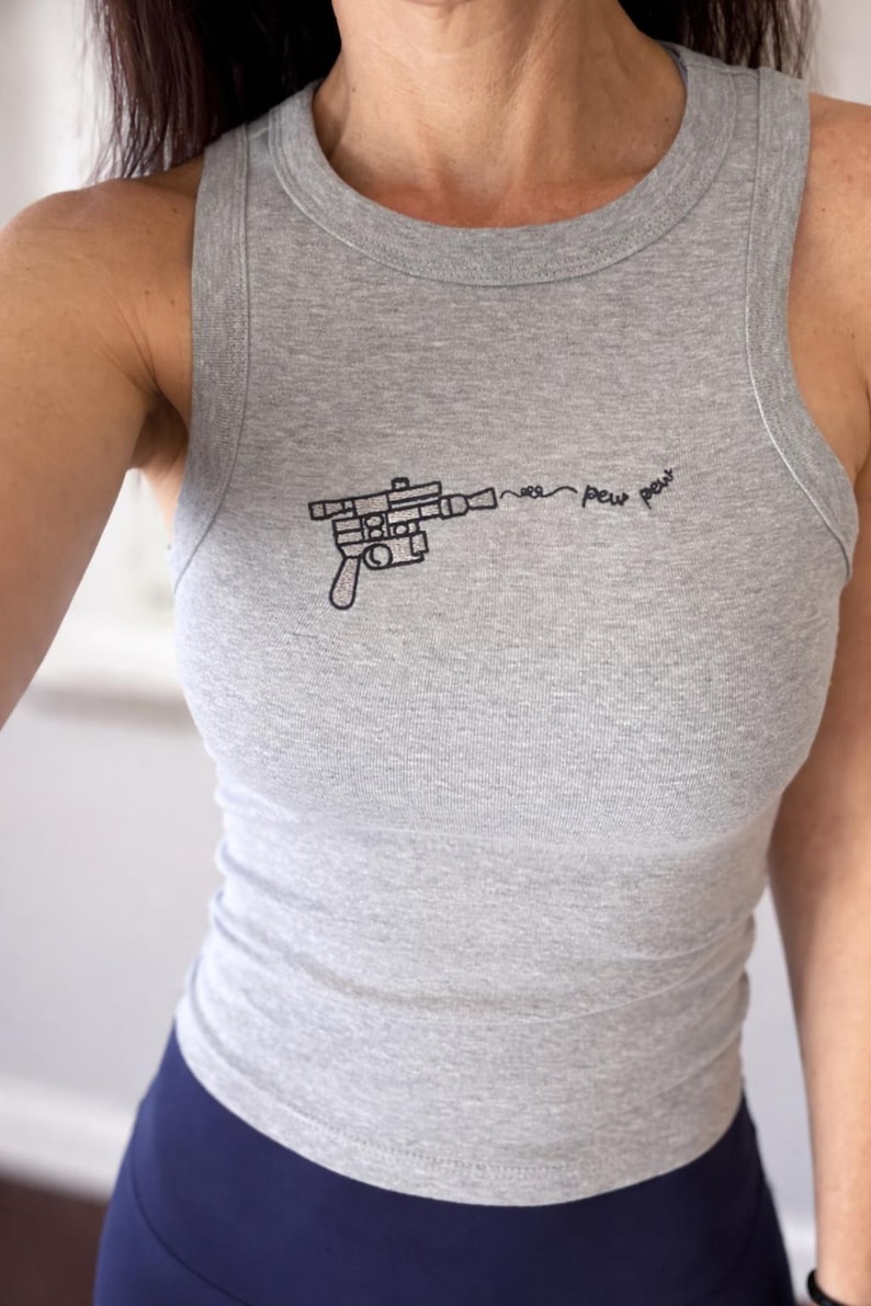 May include: A heather gray sleeveless tank top featuring a black embroidered graphic of a sci-fi blaster pistol. The design includes a stylized trail of smoke and the text "pew pew" extending from the barrel of the weapon in a thin, cursive font.