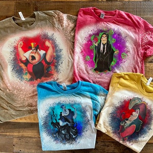 May include: Four bleach-splattered t-shirts with different Disney villains printed on them. The shirts are in various colors, including brown, red, blue, and yellow. The villains include the Queen of Hearts, Maleficent, Ursula, and Captain Hook.