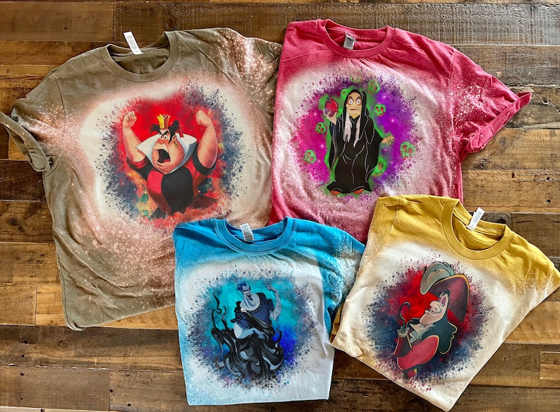 May include: Four bleach-splattered t-shirts with different Disney villains printed on them. The shirts are in various colors, including brown, red, blue, and yellow. The villains include the Queen of Hearts, Maleficent, Ursula, and Captain Hook.