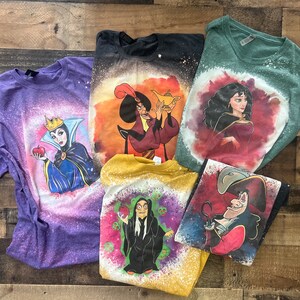 May include: Five different t-shirts with bleach-splattered designs featuring Disney villains. The shirts are purple, black, green, yellow, and blue. The villains featured are Maleficent, Jafar, Ursula, Cruella de Vil, and Captain Hook.
