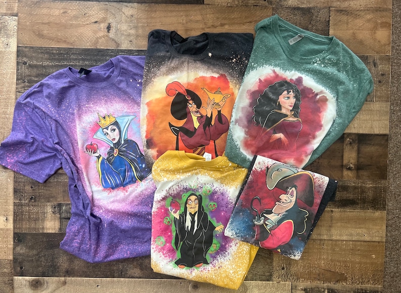 May include: Five different t-shirts with bleach-splattered designs featuring Disney villains. The shirts are purple, black, green, yellow, and blue. The villains featured are Maleficent, Jafar, Ursula, Cruella de Vil, and Captain Hook.