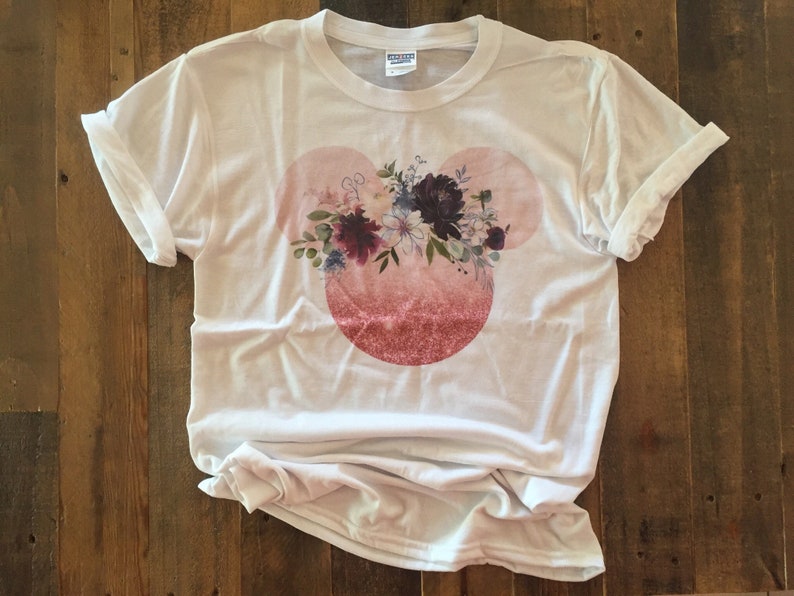 May include: White t-shirt with a pink and white floral design in the shape of Mickey Mouse ears.