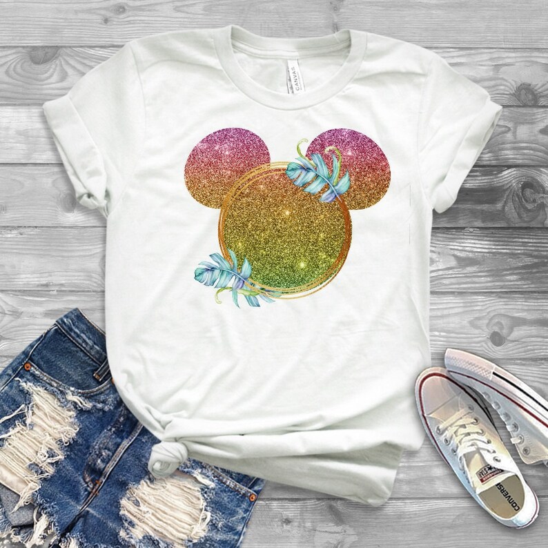May include: White t-shirt with a glitter Mickey Mouse head design featuring a gold circle and tropical leaves. The Mickey Mouse ears are pink, orange, and yellow.