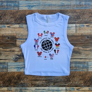 May include: A white crop top with a graphic design featuring a globe and the phrase "Conquering the World One Drink at a Time." The design includes flags of various countries. The top is sleeveless.