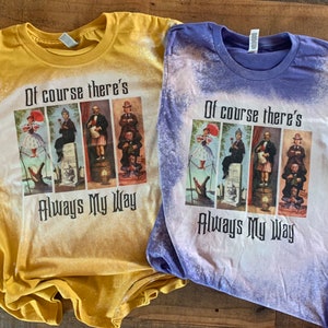 May include: Two bleached t-shirts featuring a graphic print of four characters from the film "Mary Poppins Returns". The text "Of course there's always my way" is printed below the characters. The t-shirts are yellow and purple.