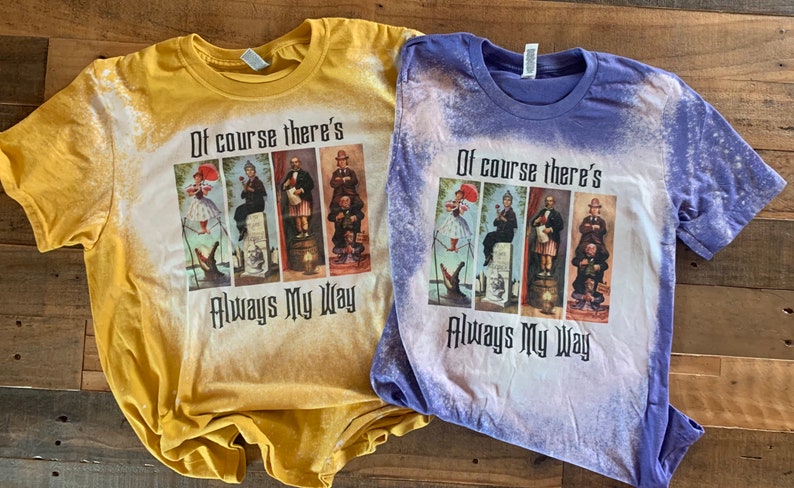 May include: Two bleached t-shirts featuring a graphic print of four characters from the film "Mary Poppins Returns". The text "Of course there's always my way" is printed below the characters. The t-shirts are yellow and purple.